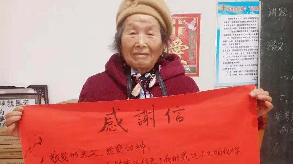 Eldre kvinne holder fram et stort, rødfarget takkebrev - en kvadratmeter stort.