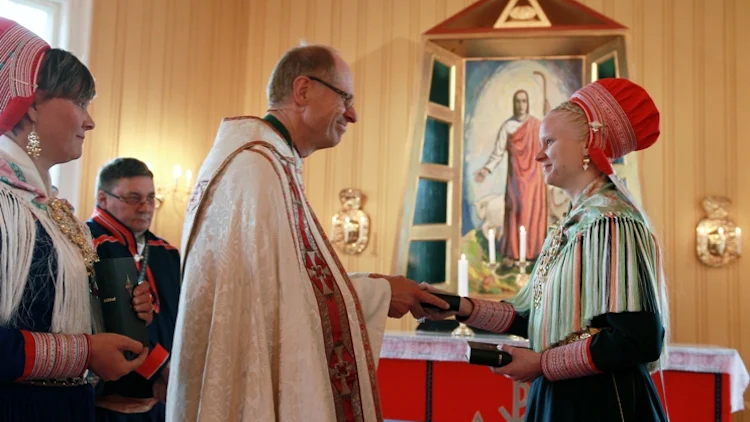 Biskop Olav Øygard blir overrakt Bibelen av Elle Karen Inga Skum. Hun har vært med i oversettelsesarbeidet, og representerte Bibelselskapet ved høytideligheten i Kautokeino kirke.