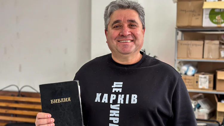 Ilya Herasym smiler fra en kirke, og viser fram en ukrainsk bibel.