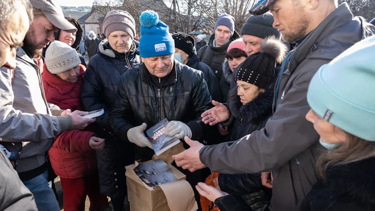 Mennesker flokker seg rundt Bibelselskapets medarbeider som deler ut bibler i en by ved frontlinjene for krigen.