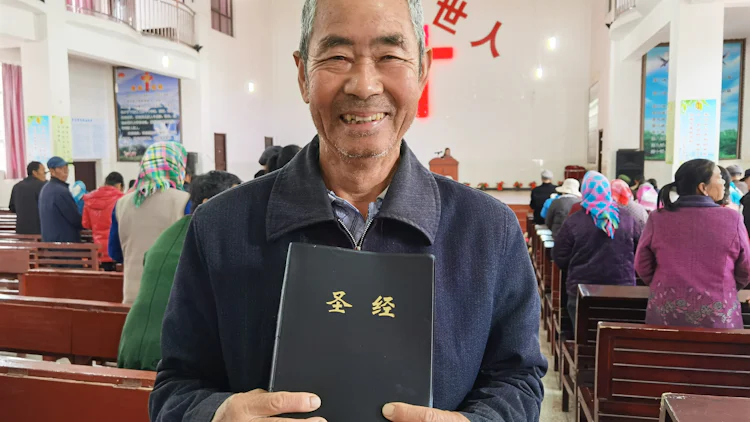 Smilende eldre mann (Gao Xuebiao) holder fram et eksemplar av Bibelen i en kinesisk kirke.